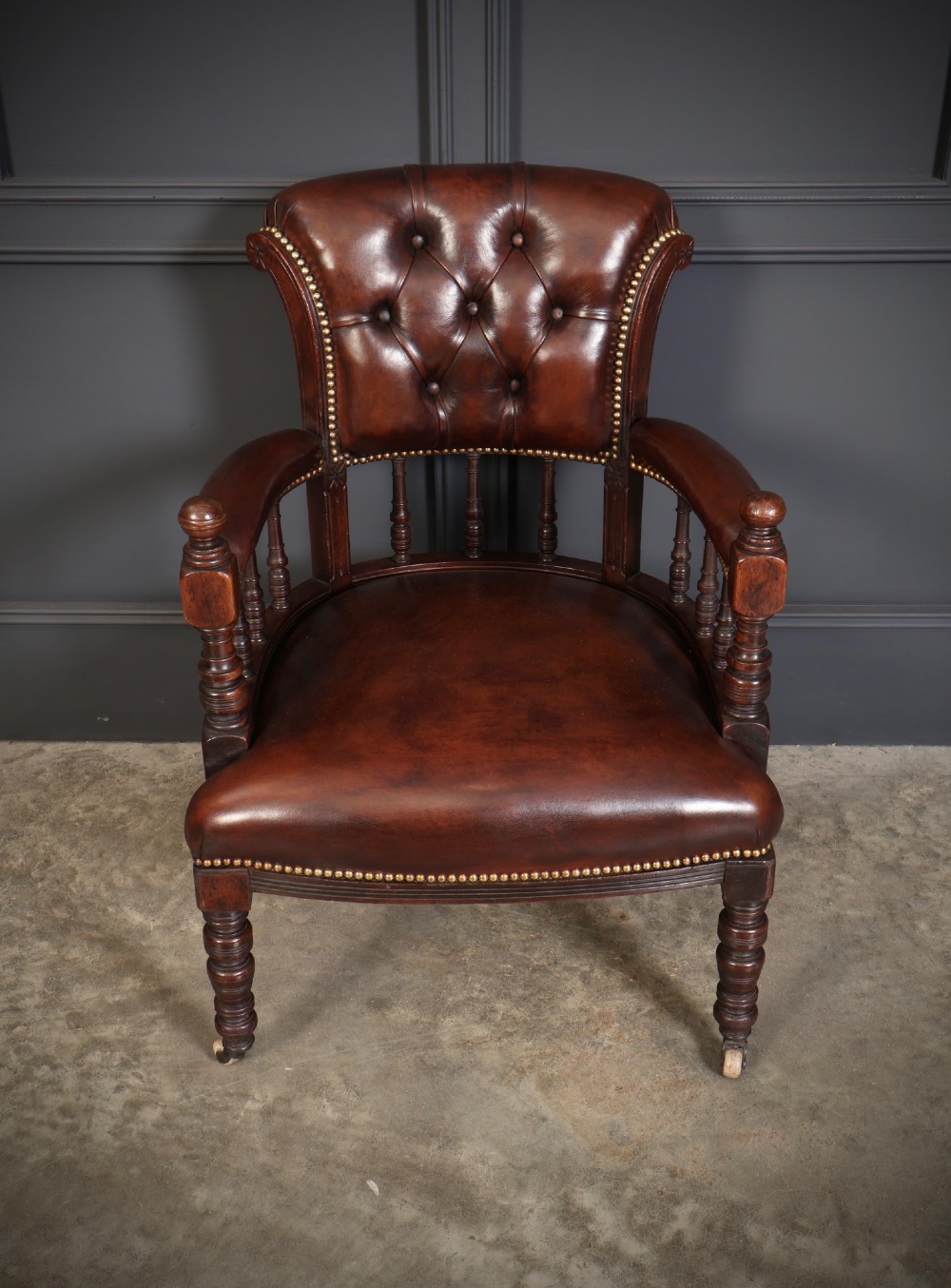 Pair of Victorian mahogany desk chairs with buttoned chestnut brown leather upholstery, brass studding, turned spindles, and castors. View VII