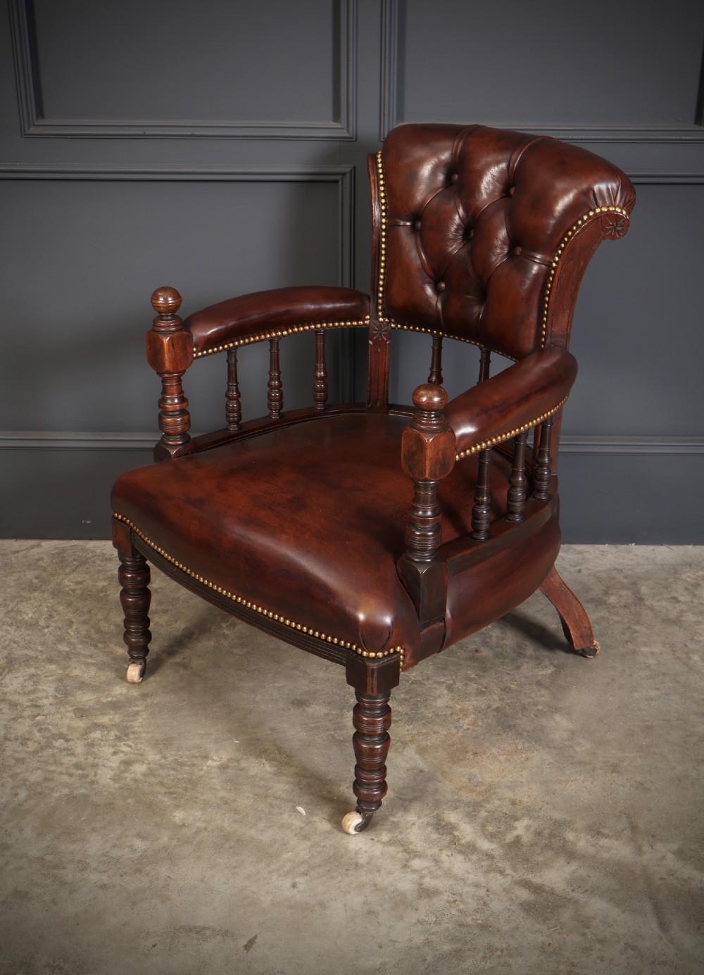 Pair of Victorian mahogany desk chairs with buttoned chestnut brown leather upholstery, brass studding, turned spindles, and castors. View VIII