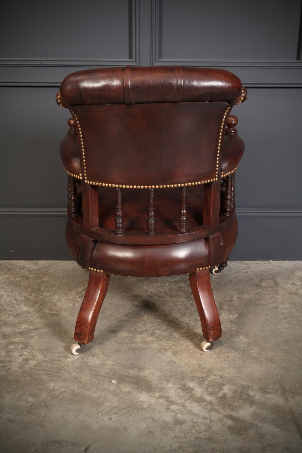 Pair of Victorian mahogany desk chairs with buttoned chestnut brown leather upholstery, brass studding, turned spindles, and castors. View X
