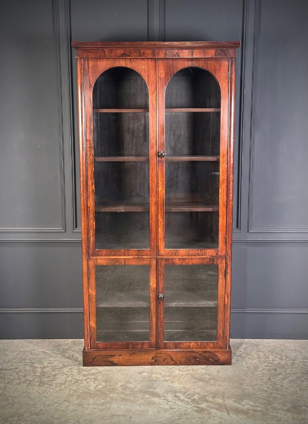 A tall Victorian rosewood bookcase featuring two upper arched glass doors and two lower glass doors on a flat plinth base. View II