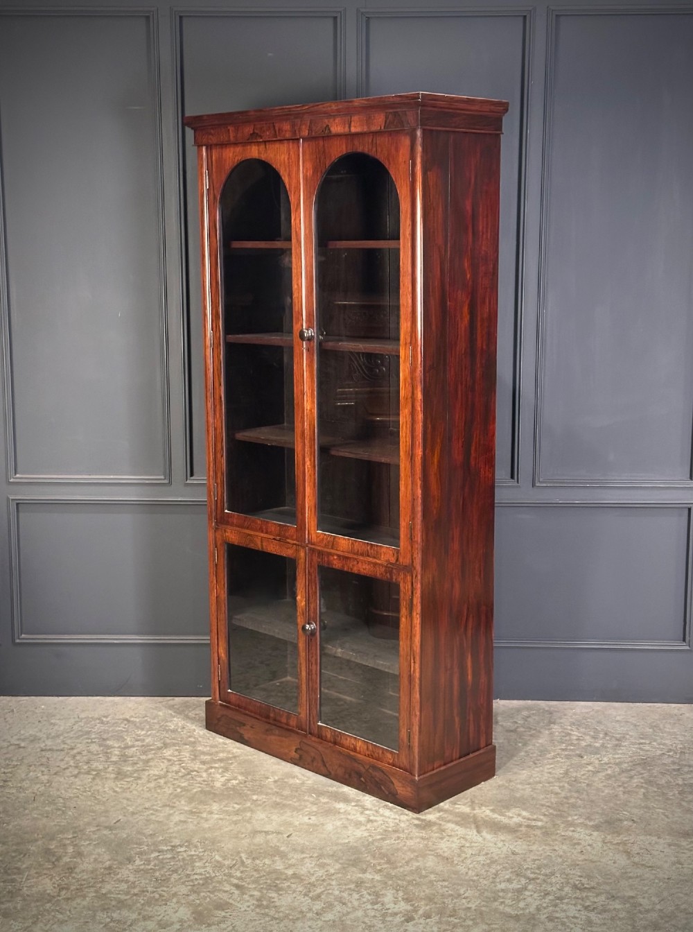 A tall Victorian rosewood bookcase featuring two upper arched glass doors and two lower glass doors on a flat plinth base. View IV