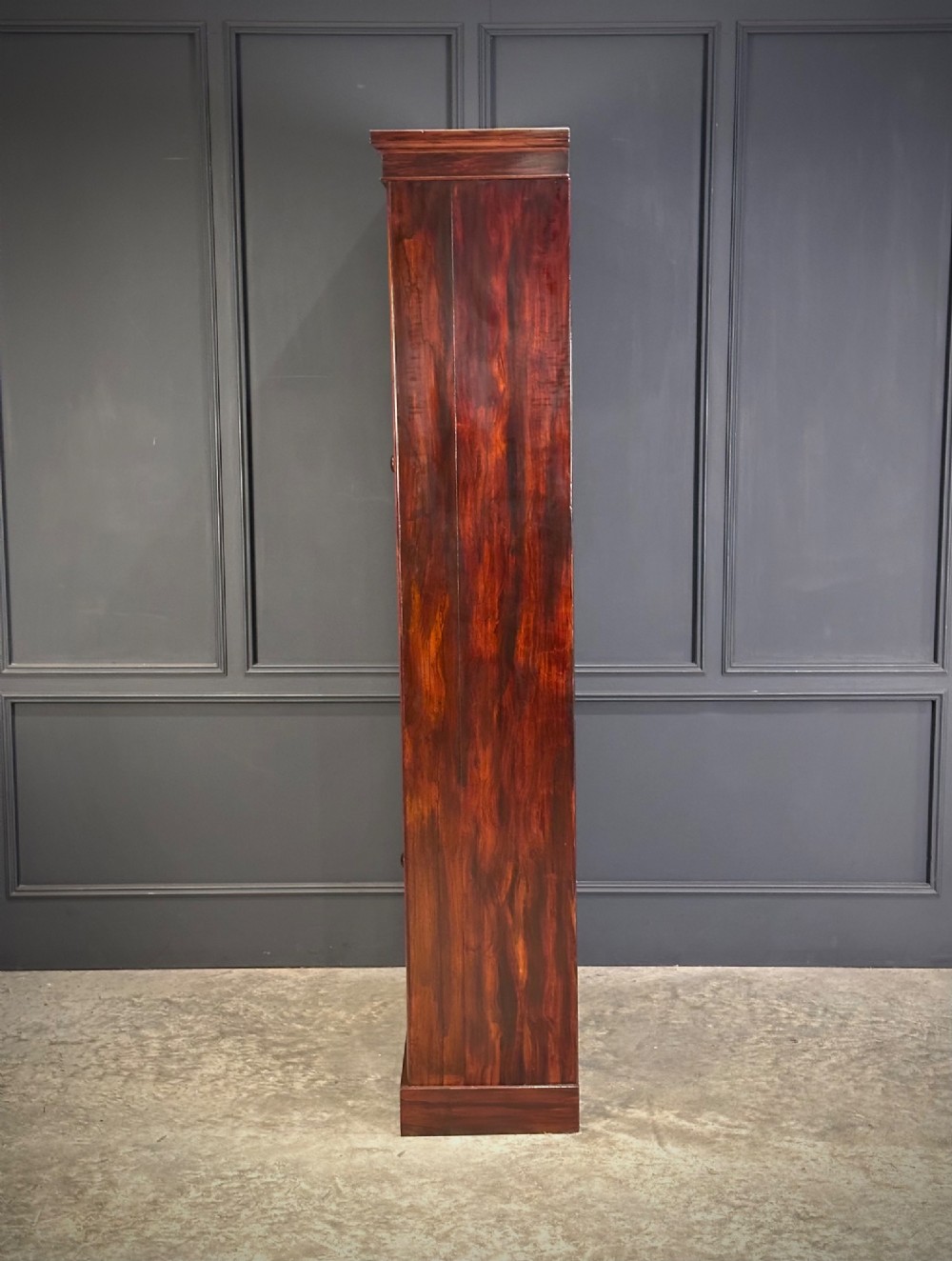 A tall Victorian rosewood bookcase featuring two upper arched glass doors and two lower glass doors on a flat plinth base. View V