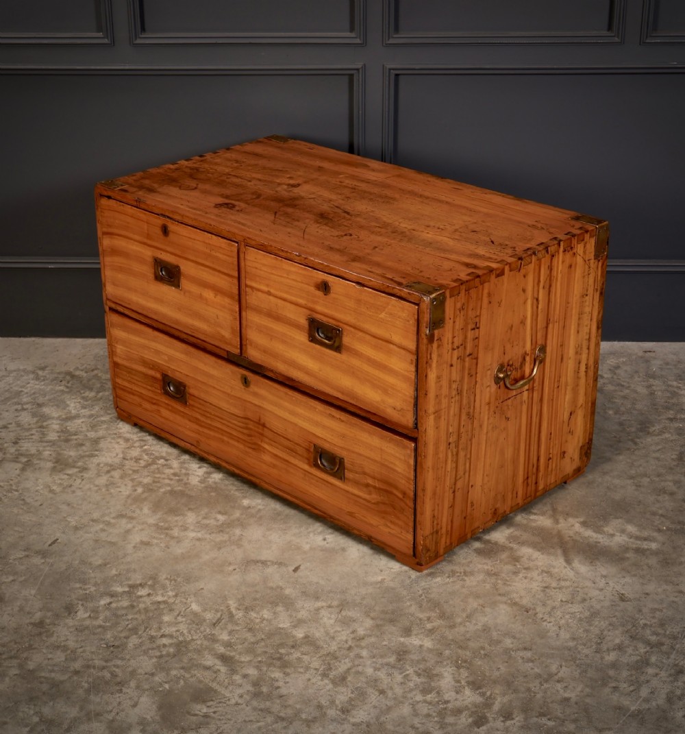 A low rectangular camphor wood campaign chest featuring three drawers with recessed brass handles, brass corner straps, and side carrying handles. View V