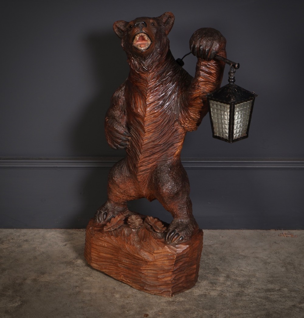 A dark hand-carved timber standing bear sculpture holding an iron lantern light fixture on a textured wooden base. View V