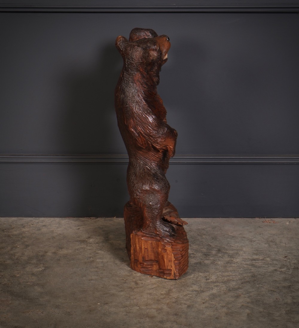 A dark hand-carved timber standing bear sculpture holding an iron lantern light fixture on a textured wooden base. View VII