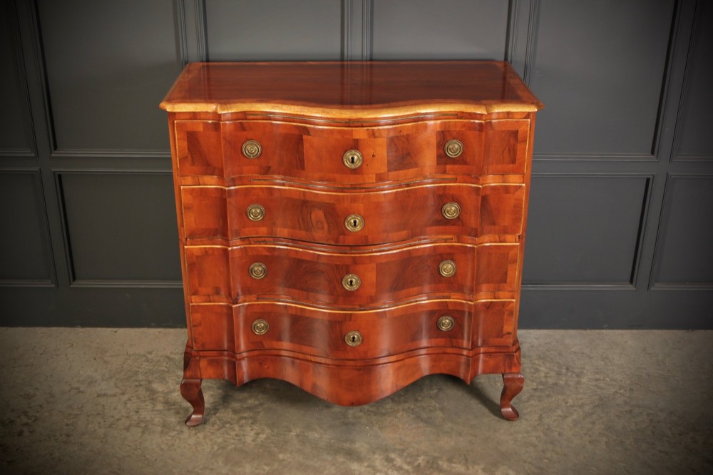 An antique walnut chest of drawers featuring a serpentine curved front, four graduated drawers with brass handles, and carved cabriole legs.