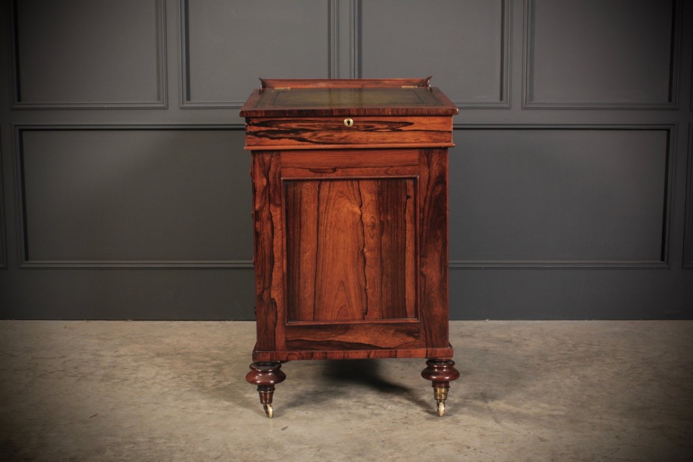 A William IV rosewood Davenport desk featuring a sloped leather writing surface, side drawers with turned knobs, and turned feet on castors. View V
