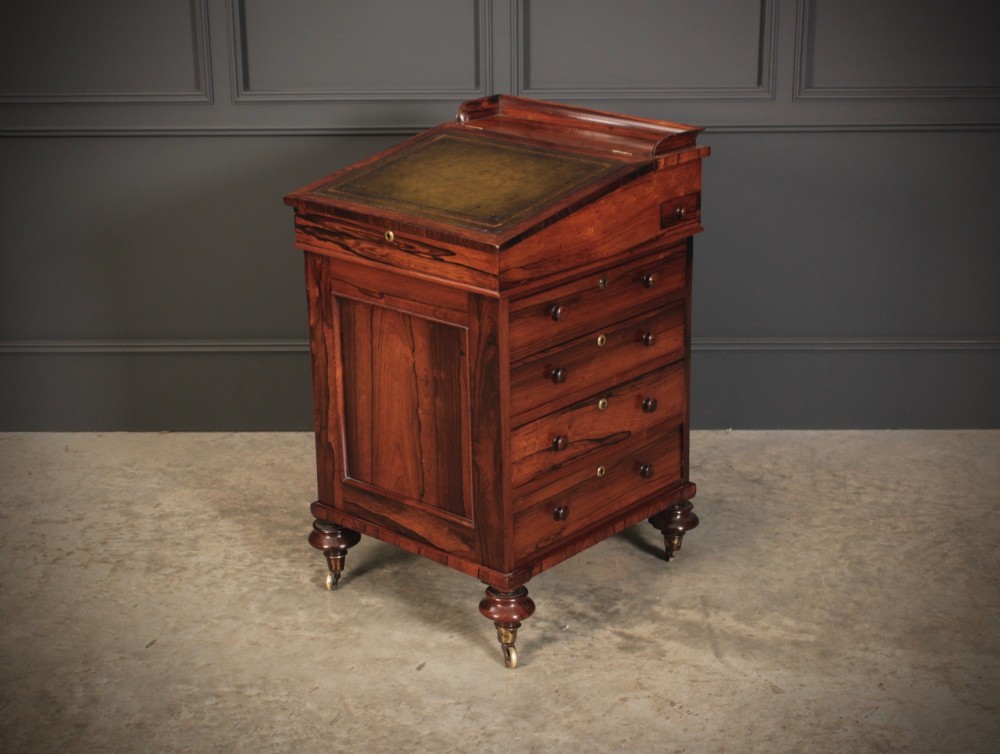 A William IV rosewood Davenport desk featuring a sloped leather writing surface, side drawers with turned knobs, and turned feet on castors.