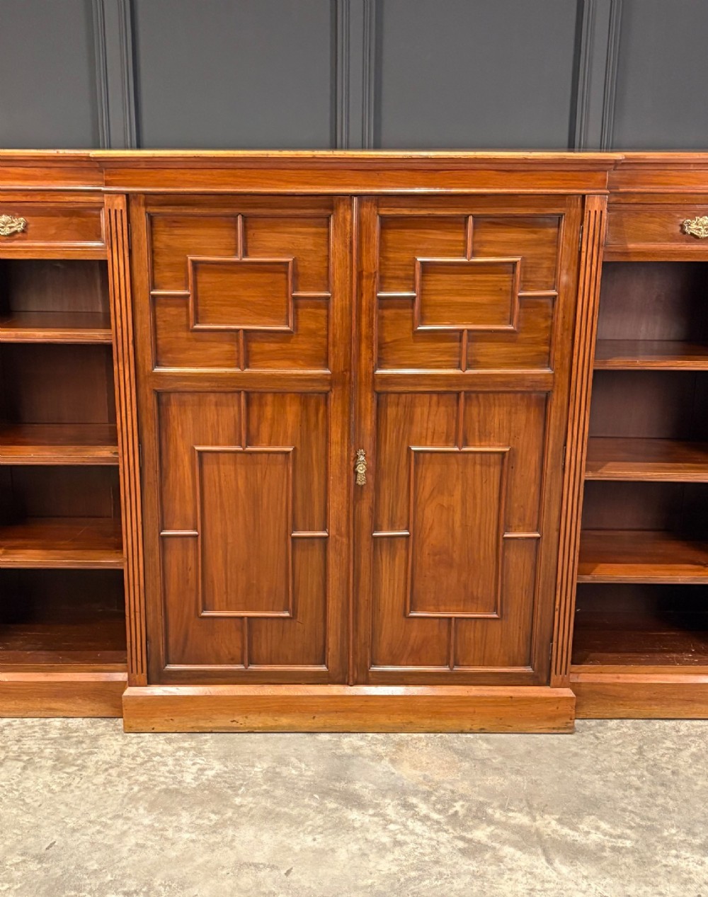 An antique Edwardian walnut breakfront bookcase with a central section featuring geometric panelled doors flanked by open adjustable shelving. View IV