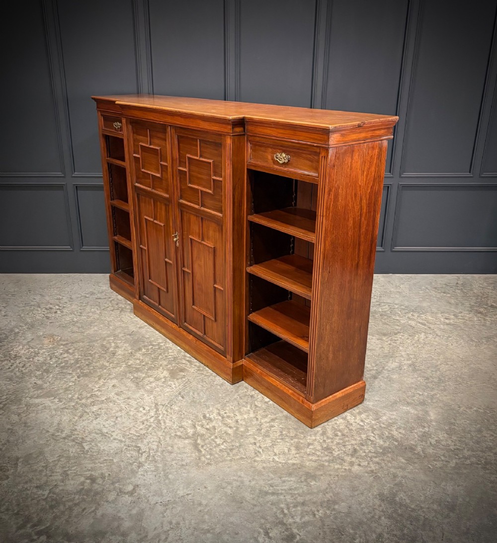 An antique Edwardian walnut breakfront bookcase with a central section featuring geometric panelled doors flanked by open adjustable shelving. View VIII