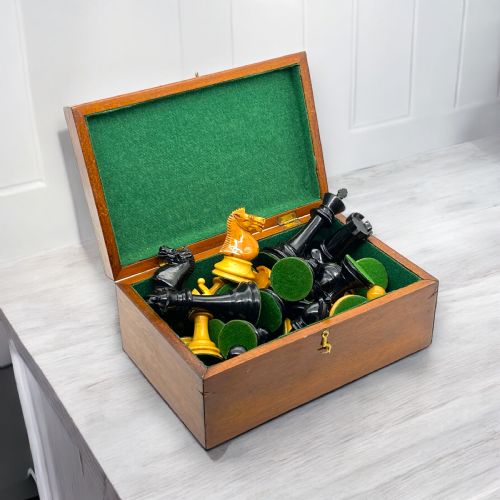 fig 1. A boxwood and ebony Staunton chess set featuring carved chessmen displayed in and around an open mahogany wooden storage box lined with green felt.