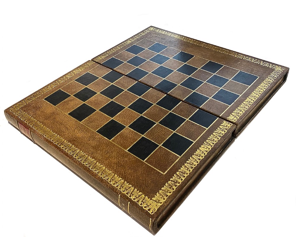 A brown leather folding chess board fashioned to resemble a vintage book with gold gilt tooling along the perimeter.