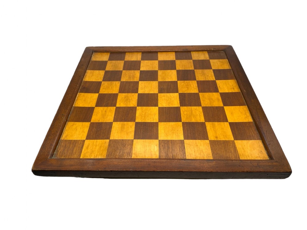 A square antique wooden chess board with alternating light and dark wood playing squares surrounded by a dark timber border frame.