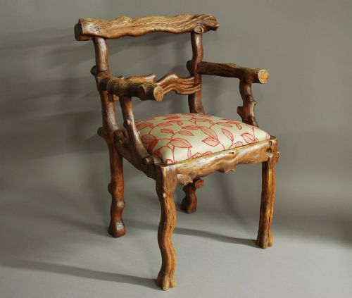fig 1. A mid-19th-century carved elm armchair featuring a branch-like naturalistic wooden frame and a cream upholstered seat with red leaf motifs.