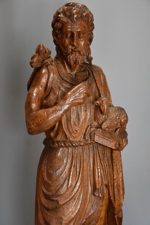 fig 1. A 16th-century carved limewood figure of St. John the Baptist holding a lamb, mounted on a dark wooden base.