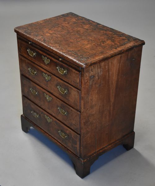 fig 1. An early 18th-century walnut chest of drawers featuring four graduated drawers, brass drop handles, keyhole escutcheons, a brushing slide, and bracket feet.