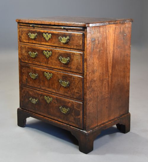 fig 2. An early 18th-century walnut chest of drawers featuring four graduated drawers, brass drop handles, keyhole escutcheons, a brushing slide, and bracket feet.