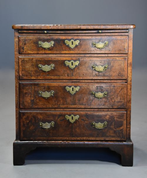 fig 3. An early 18th-century walnut chest of drawers featuring four graduated drawers, brass drop handles, keyhole escutcheons, a brushing slide, and bracket feet.