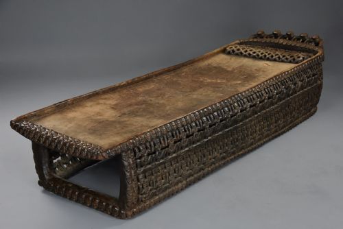 fig 2. A long hand-carved dark hardwood Bamileke ceremonial bed featuring intricate openwork figurative carvings along the frame and an integrated raised headrest.