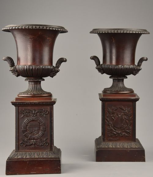 fig 1. A pair of dark brown patinated spelter campana urns featuring gadrooned bases, scroll handles, and square stepped plinths with relief decoration.