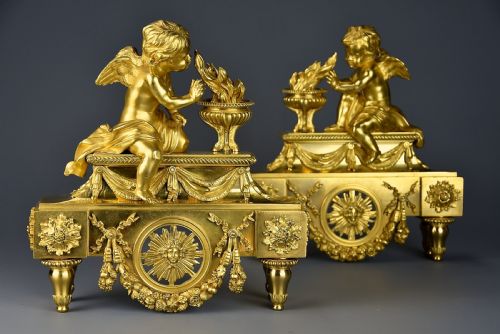 fig 1. A pair of late nineteenth-century gilded bronze fire dogs featuring seated winged cherubs warming their hands by flaming urns above solar masks and drapery.