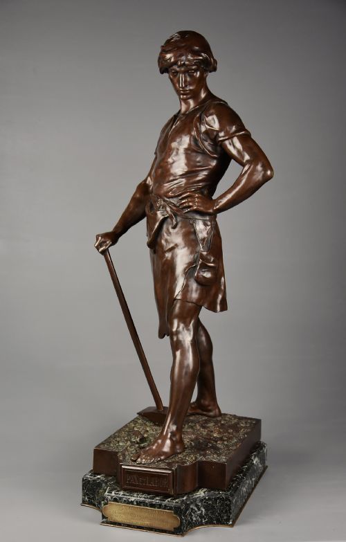 fig 1. A dark brown patinated bronze sculpture of a standing male figure resting on a rectangular marble base with an etched metal title plaque.