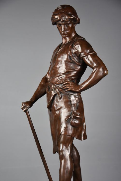 fig 2. A dark brown patinated bronze sculpture of a standing male figure resting on a rectangular marble base with an etched metal title plaque.
