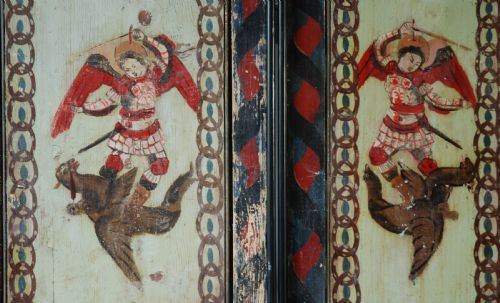 fig 1. A set of four rectangular vertical pine panels decorated with naive paintings of Saint Michael slaying a winged dragon within chainlink borders.