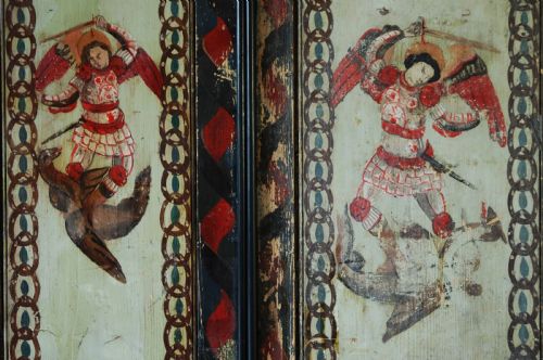 fig 2. A set of four rectangular vertical pine panels decorated with naive paintings of Saint Michael slaying a winged dragon within chainlink borders.