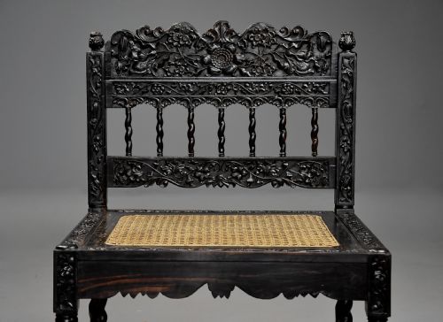 fig 3. A 17th-century dark carved ebony low chair featuring floral relief carving on the frame, a hand-woven cane seat, and spiralled barley-twist legs.
