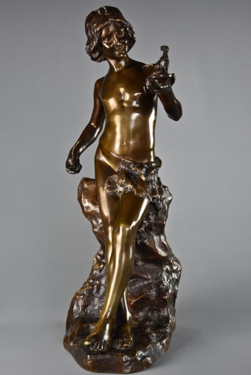 fig 1. A dark brown patinated bronze sculpture depicting a standing youth leaning against a rocky base while holding a small figurine of a goat in his raised left hand.
