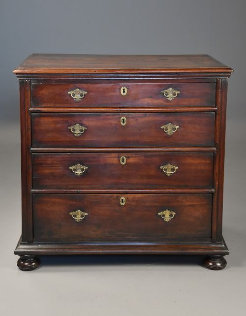 fig 1. A late seventeenth-century fruitwood chest of drawers featuring four graduated drawers with brass drop handles, brass escutcheons, panelled sides, and bun feet.