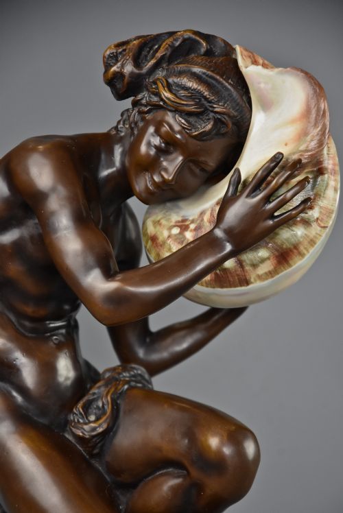 fig 1. A patinated dark bronze sculpture depicting a youth kneeling and holding a large seashell to his ear on an octagonal base.