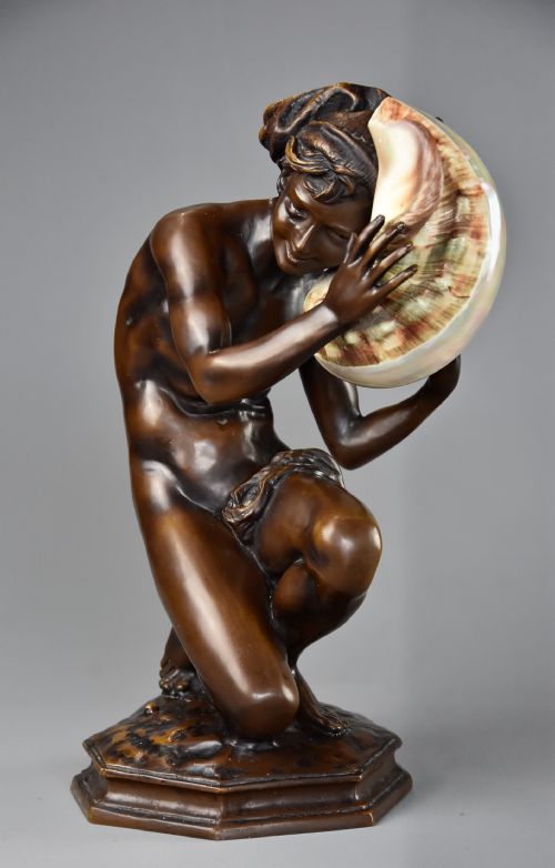 fig 2. A patinated dark bronze sculpture depicting a youth kneeling and holding a large seashell to his ear on an octagonal base.