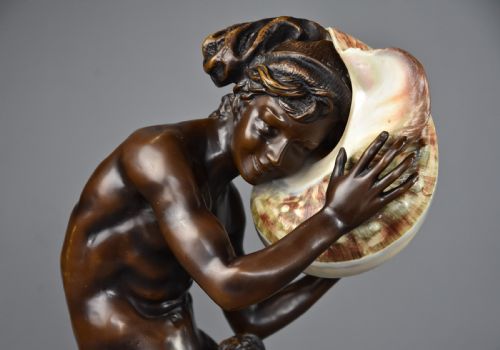 fig 3. A patinated dark bronze sculpture depicting a youth kneeling and holding a large seashell to his ear on an octagonal base.