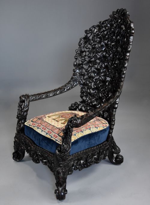 fig 4. A 19th-century Anglo-Indian carved blackwood armchair featuring an intricately pierced foliate backrest and an embroidered fabric seat cushion.