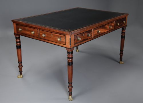 fig 1. A Regency mahogany writing table featuring a dark leather insert, six drawers with brass knobs, and reeded turned legs with brass paw feet.