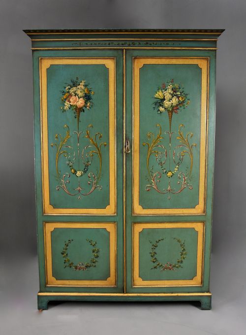 fig 2. An early twentieth-century hand-painted green and gold bedroom suite featuring a wardrobe, chest of drawers with mirror, dressing desk, side tables, and caned chairs decorated with floral urn motifs.