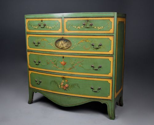 fig 8. An early twentieth-century hand-painted green and gold bedroom suite featuring a wardrobe, chest of drawers with mirror, dressing desk, side tables, and caned chairs decorated with floral urn motifs.
