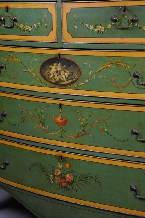 fig 10. An early twentieth-century hand-painted green and gold bedroom suite featuring a wardrobe, chest of drawers with mirror, dressing desk, side tables, and caned chairs decorated with floral urn motifs.