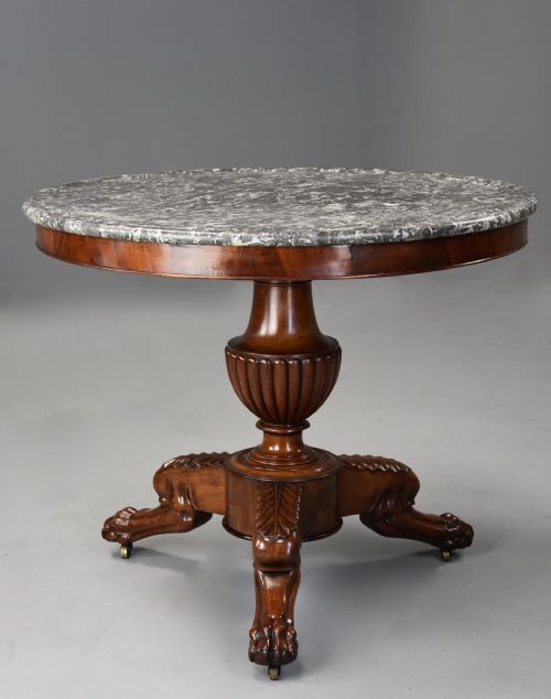fig 1. A 19th-century French circular mahogany centre table featuring a grey veined marble top resting on a turned pedestal stem with carved tripod paw legs.
