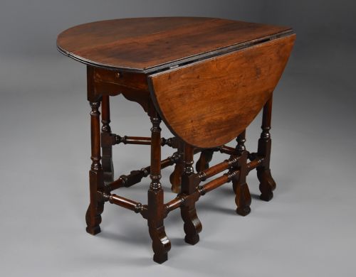 fig 1. An 18th-century red walnut gateleg table featuring an oval top with two drop leaves, turned legs, box stretchers, and a small drawer with a brass knob.