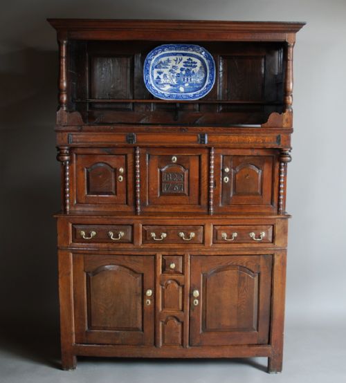 fig 1. A mid-18th-century three-tier Welsh oak cwpwrdd tridarn featuring an open top canopy, carved panel dated 1761, turned pillars, and lower cupboards.