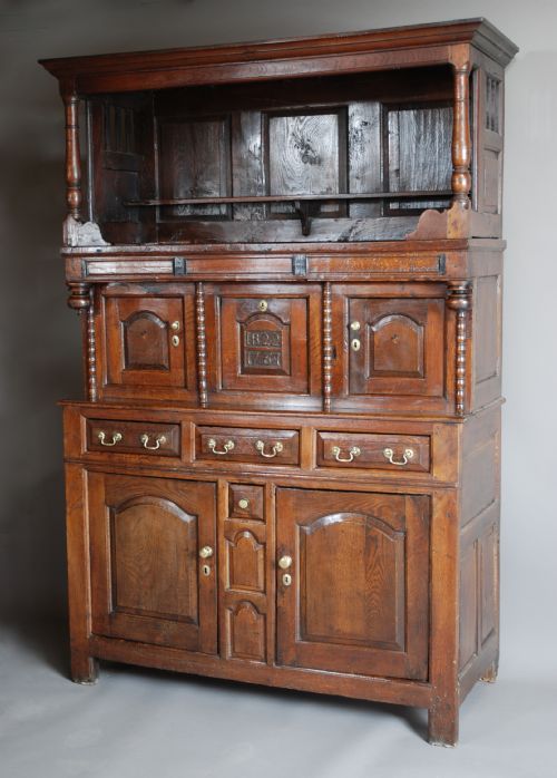 fig 2. A mid-18th-century three-tier Welsh oak cwpwrdd tridarn featuring an open top canopy, carved panel dated 1761, turned pillars, and lower cupboards.