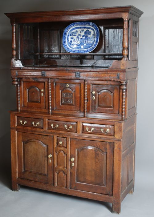fig 3. A mid-18th-century three-tier Welsh oak cwpwrdd tridarn featuring an open top canopy, carved panel dated 1761, turned pillars, and lower cupboards.