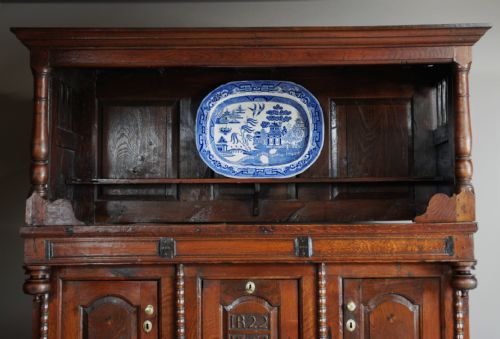 fig 4. A mid-18th-century three-tier Welsh oak cwpwrdd tridarn featuring an open top canopy, carved panel dated 1761, turned pillars, and lower cupboards.