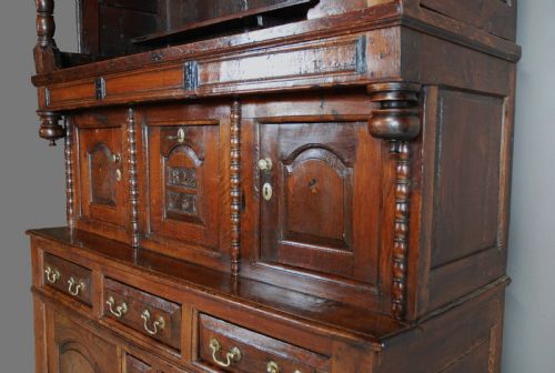 fig 5. A mid-18th-century three-tier Welsh oak cwpwrdd tridarn featuring an open top canopy, carved panel dated 1761, turned pillars, and lower cupboards.