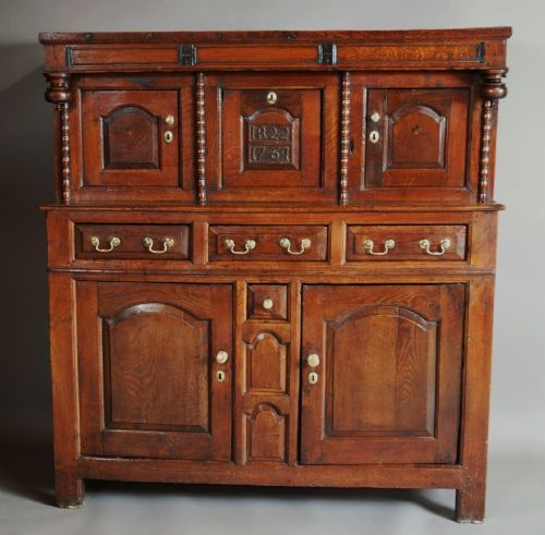 fig 6. A mid-18th-century three-tier Welsh oak cwpwrdd tridarn featuring an open top canopy, carved panel dated 1761, turned pillars, and lower cupboards.
