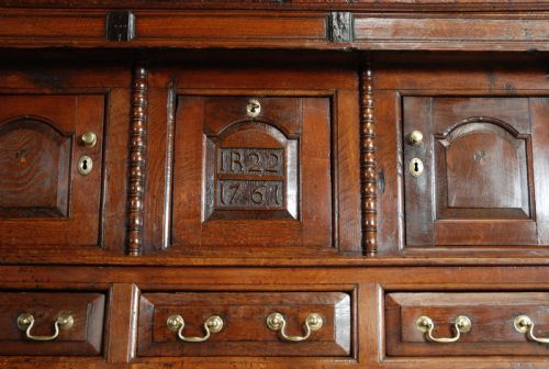 fig 7. A mid-18th-century three-tier Welsh oak cwpwrdd tridarn featuring an open top canopy, carved panel dated 1761, turned pillars, and lower cupboards.