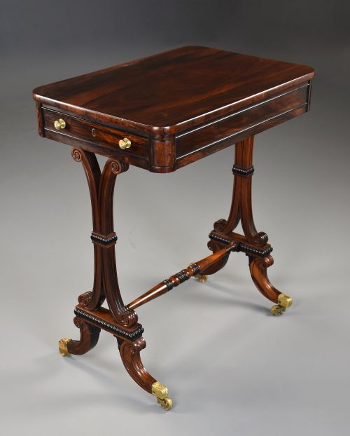 fig 1. An early nineteenth-century rosewood occasional table featuring a rectangular top with a single drawer, scrolled trestle supports, beaded mouldings, and brass castors.